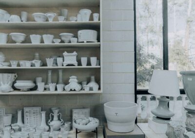 A collection of handmade ceramic items displayed on shelves in a crafts workshop, featuring bowls, vases, and a lamp.