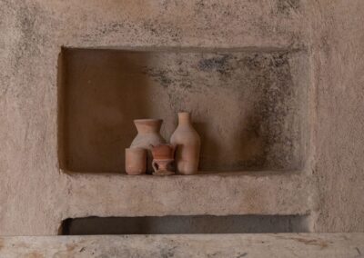 A collection of rustic clay pottery displayed on a textured wall shelf with earthy tones.
