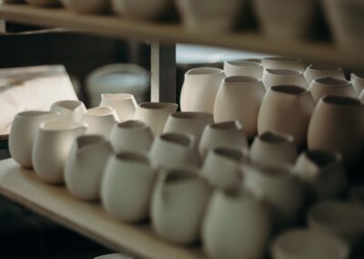Handcrafted ceramic pots and mugs showcased on wooden shelves with natural lighting.