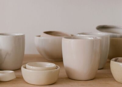 A collection of handcrafted ceramic bowls and cups in a minimalist style on a wooden table.