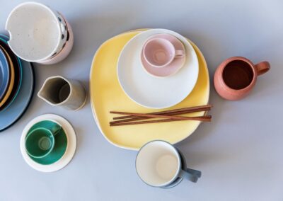 A flat lay of colorful ceramic tableware including plates, mugs, and chopsticks on a gray surface.